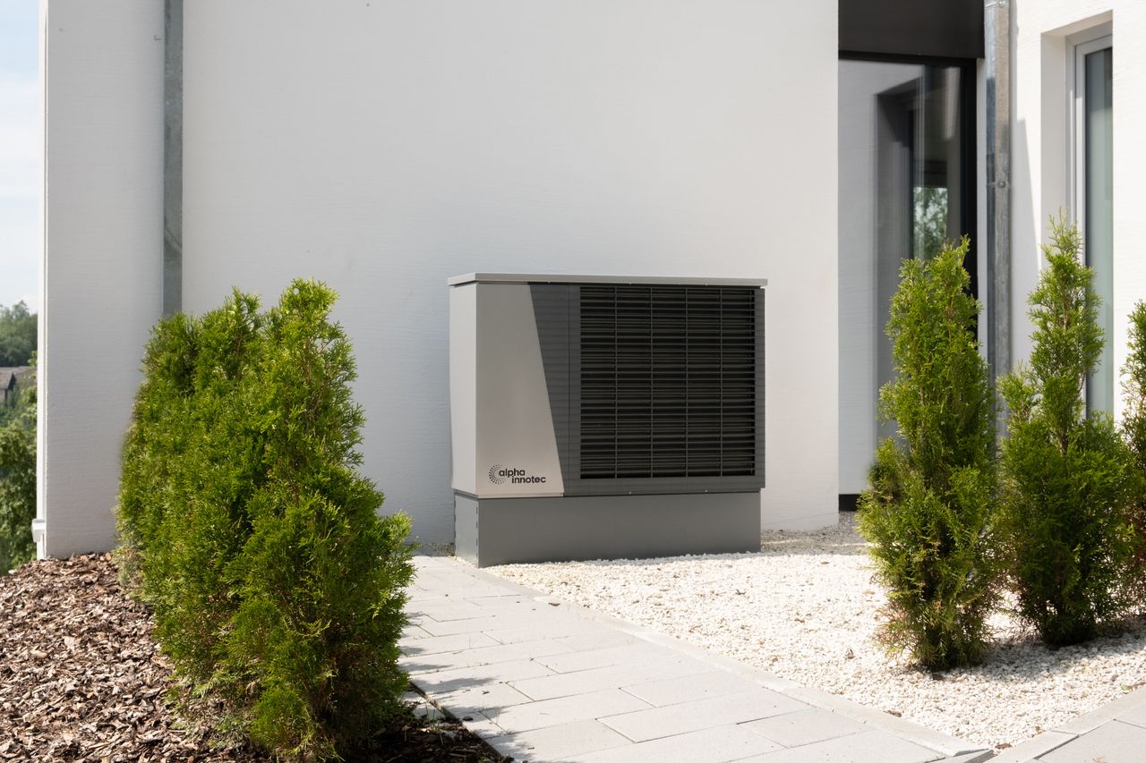 gallery-02 Outdoor air conditioner unit on a modern building surrounded by greenery and landscaping.
