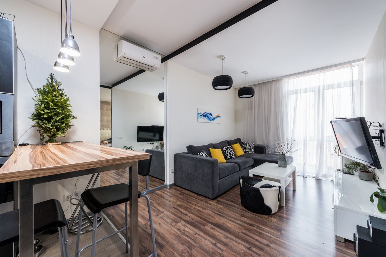 experience-01 Interior of modern spacious living room with comfy sofa and wooden counter placed near big mirror reflecting TV in daytime